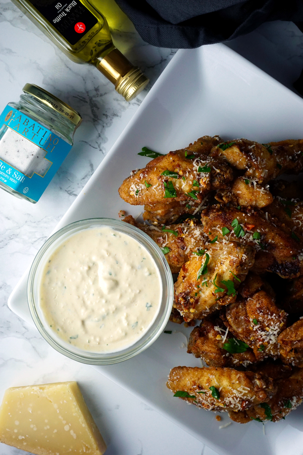 parmesan truffle chicken wings on a plate with garlic dip and a jar of truffle salt