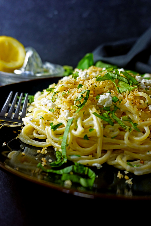 Lemon Goat Cheese Spaghetti with Toasted Pangrattato Breadcrumbs on a blue plate with basil and lemon rinds