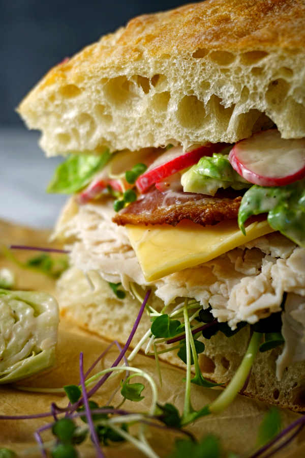 Close-up photo of a Turkey bacon club sandwich on ciabatta bread with brussel sprout slaw on a piece of parchment paper