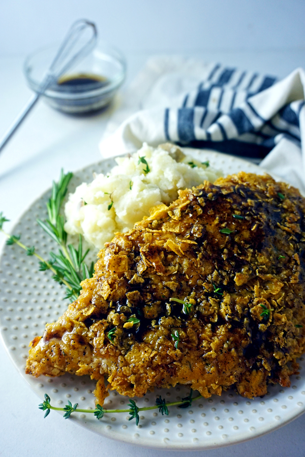 Crispy baked chicken breast coated in cornflakes on a plate with herbs and mashed potatoes