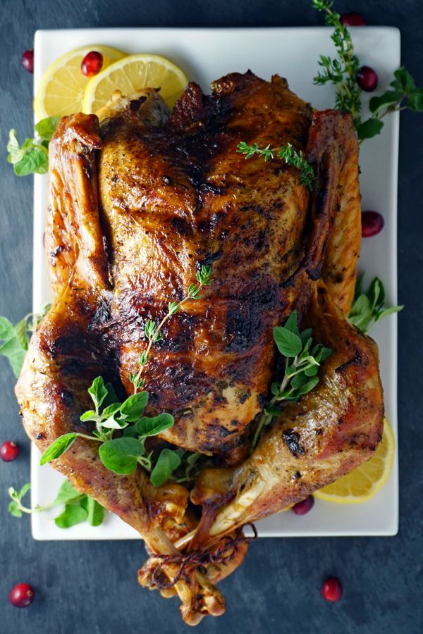 whole mayonnaise-rubbed turkey on a platter with lemon, herbs and cranberries