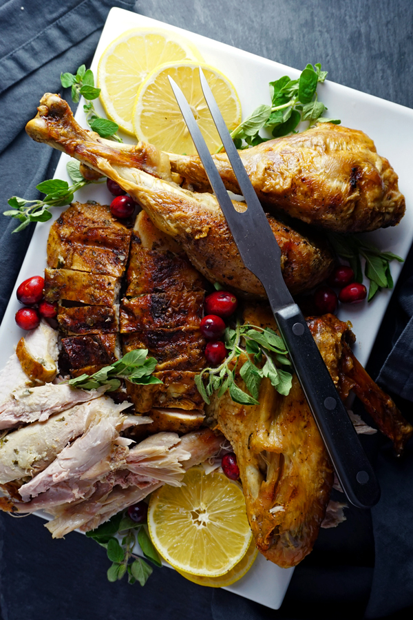 carved mayo-rubbed turkey on a platter with herbs and cranberries