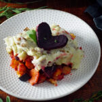 vegan root vegetable shepherd's pie on a plate garnished with a beet heart