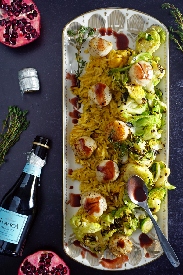 a white and gold platter of jumbo scallops pan-seared with a pomegranate prosecco sauce and served over brussel sprouts and creamy butternut squash orzo