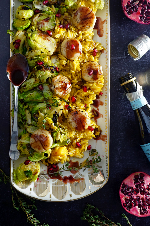 a white and gold platter of sea scallops pan-seared with a pomegranate prosecco sauce and served over brussel sprouts and creamy butternut squash orzo