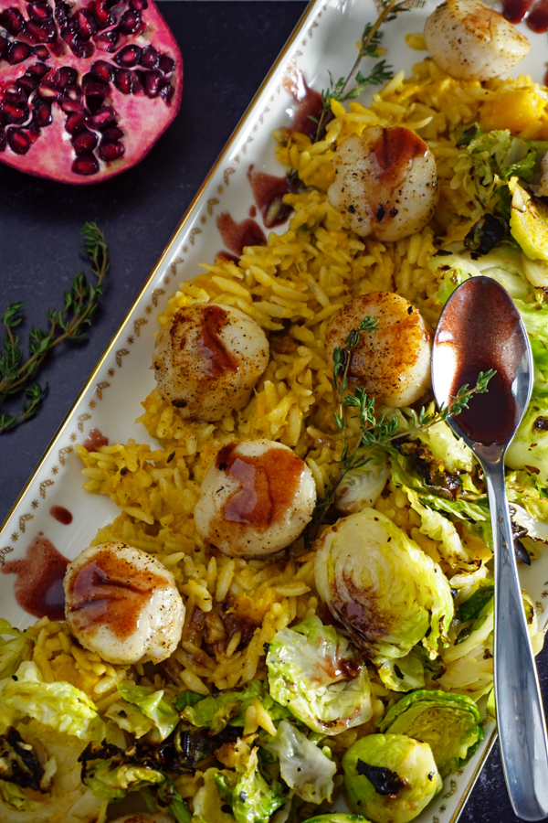 a white and gold platter of pan-seared scallops with a pomegranate prosecco sauce and served over brussel sprouts and creamy butternut squash orzo