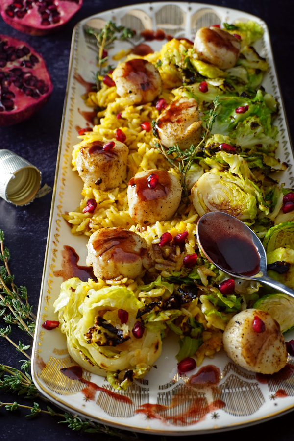 a white and gold platter of sea scallops pan-seared with a pomegranate prosecco sauce and served over brussel sprouts and creamy butternut squash orzo