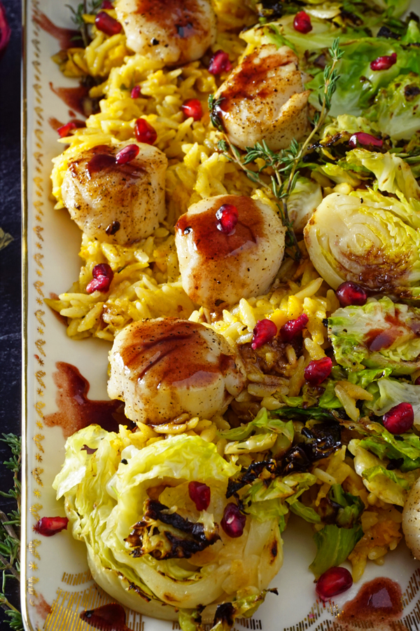 a white and gold platter of scallops pan-seared with a pomegranate prosecco sauce and served over brussel sprouts and creamy butternut squash orzo