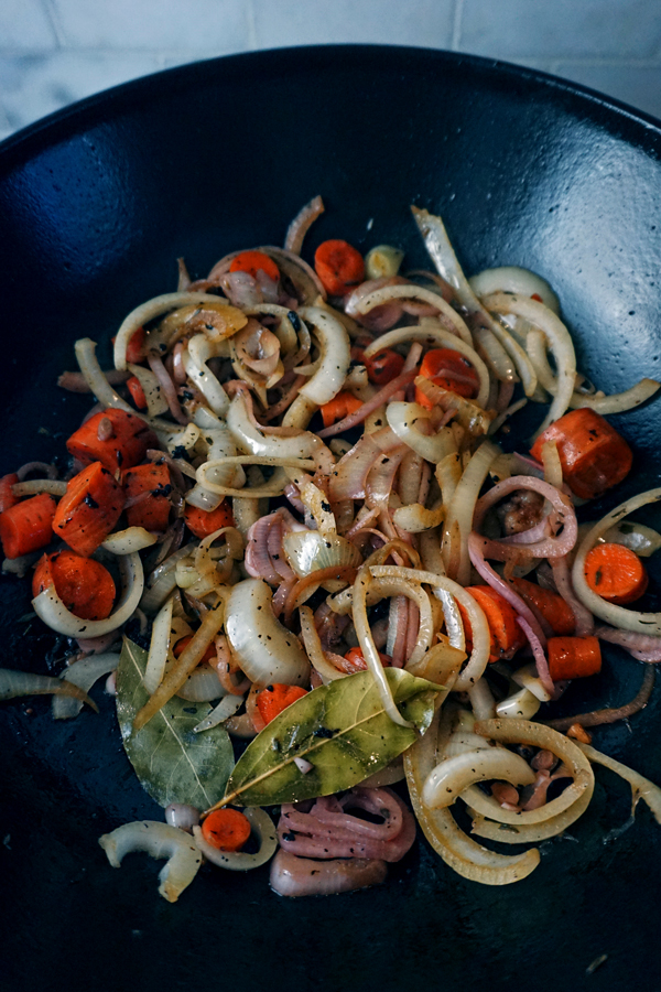 onions, carrots and herbs being sautéed in a pan for sauerbraten