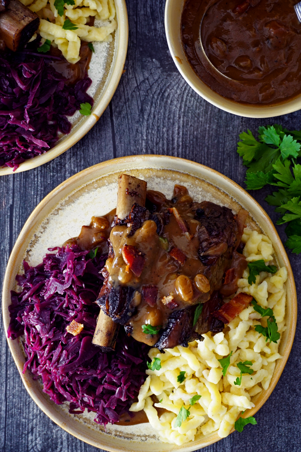 braised beef short ribs prepared as sauerbraten on a plate withred cabbage, gravy and spätzle overhead