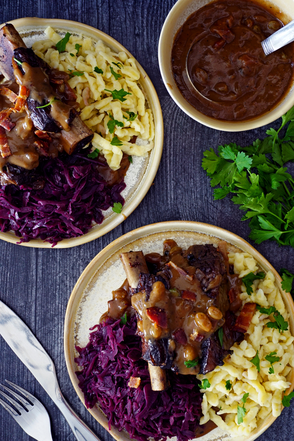 two plates overhead of braised beef short ribs prepared as german sauerbraten with red cabbage, gravy and spätzle