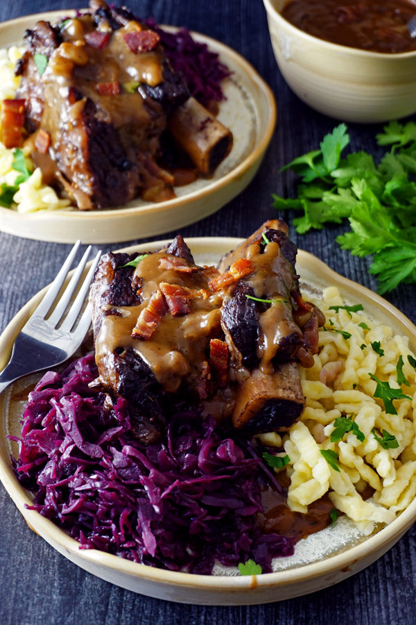 braised beef short ribs prepared as sauerbraten on a plate withred cabbage, gravy and spätzle