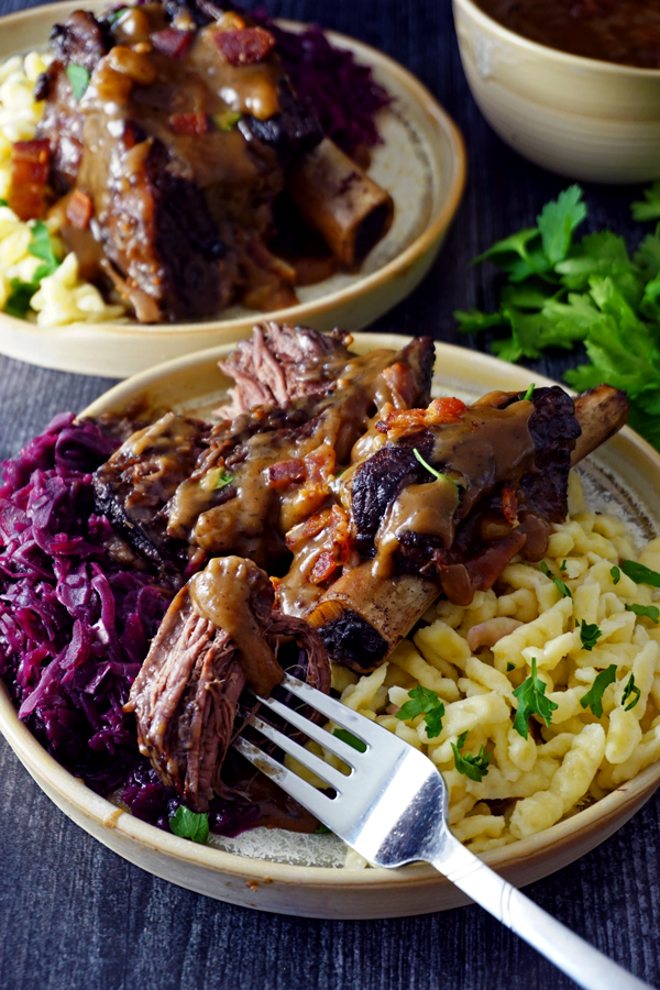 A tender piece of braised sauerbraten short ribs on a fork with red cabbage and gravy