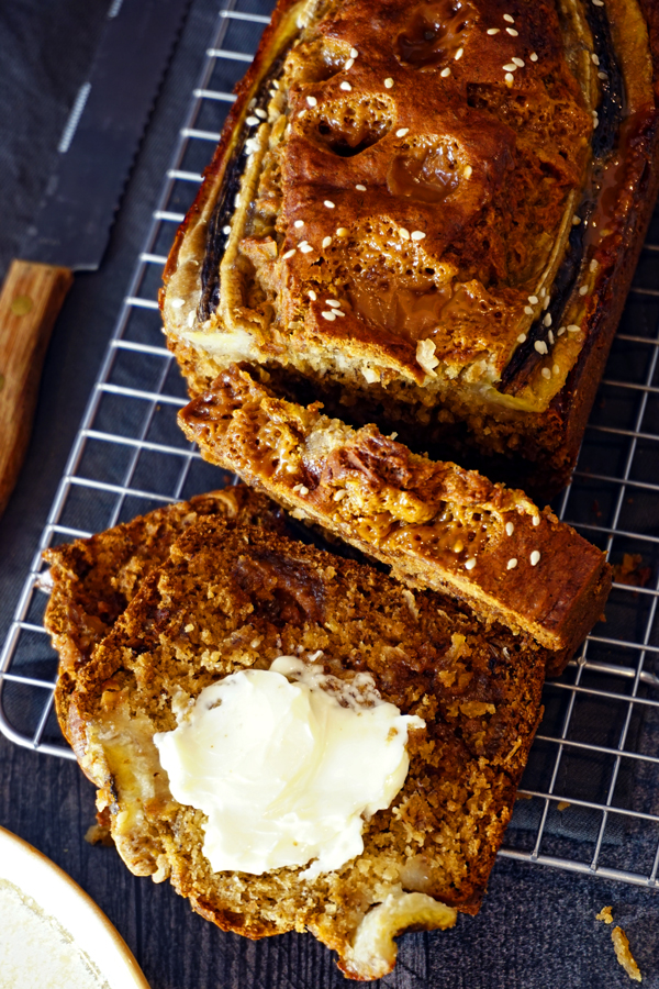 A loaf of banana bread cut into slices with butter on a wire cooling rack