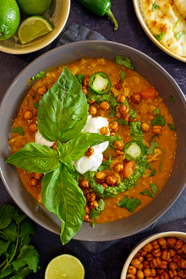 colorful tikka masala soup with green chutney in a grey bowl with yogurt and basil