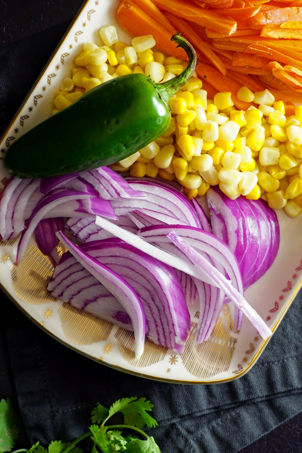 shredded carrots, corn kernels, sliced red onions and a whole fresh jalapeno on a decorative platter 