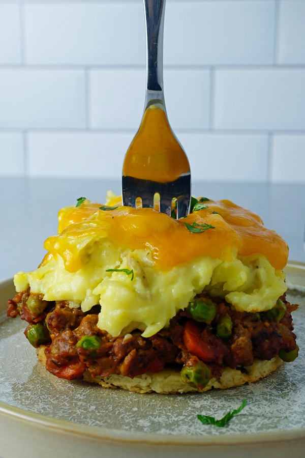 a fork stabbing an individual shepherd's pie topped with melted cheddar cheese