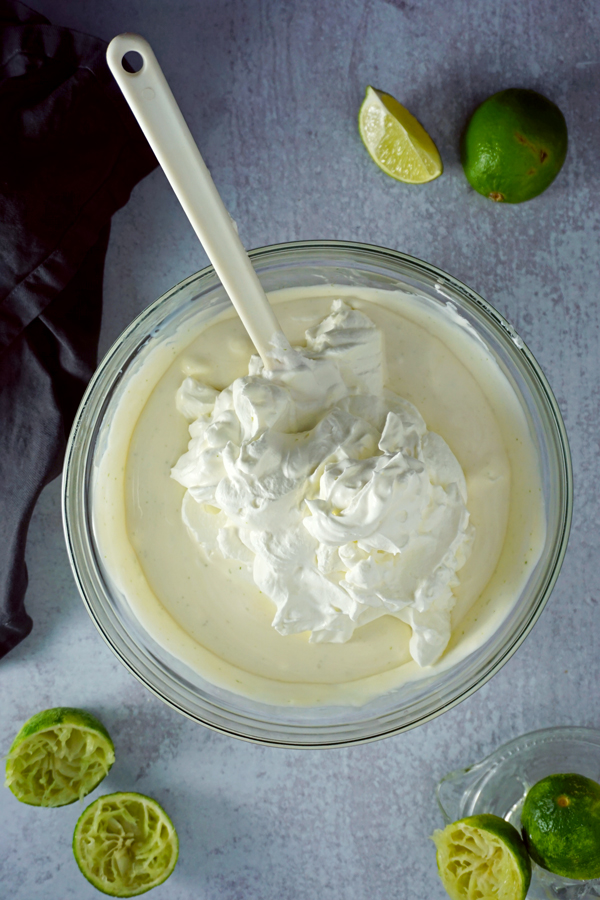 adding whipped cream to the moscow mule ice cream base in a glass mixing bowl