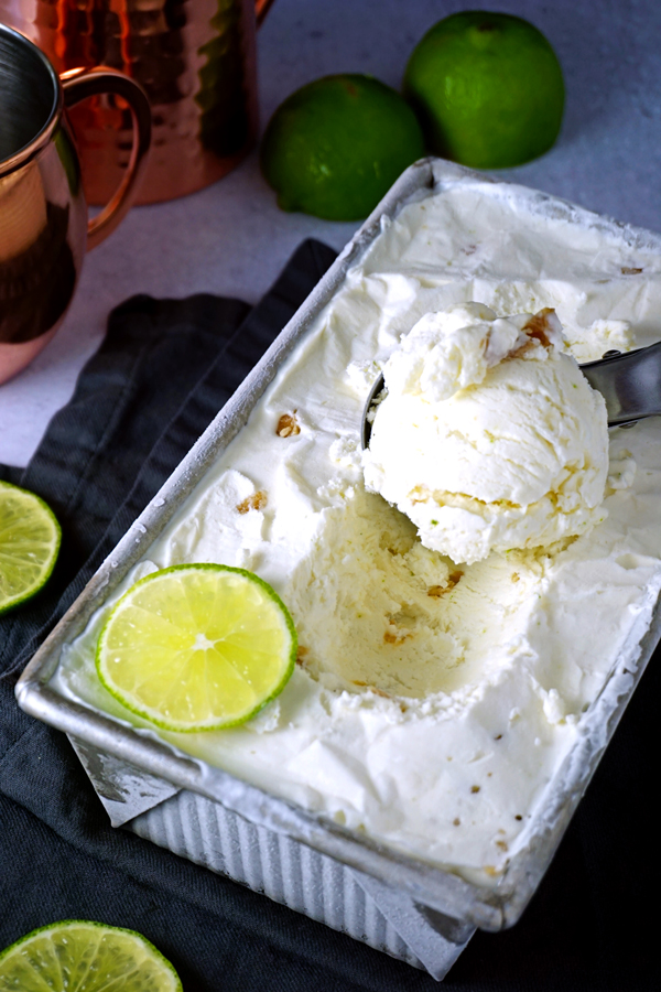 finished frozen moscow mule no-churn ice cream garnished with limes in a loaf pan with an ice cream scoop